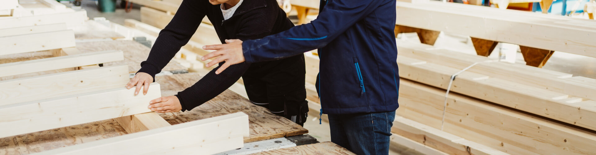 Zimmerer-Team bespricht Holzbauprojekt in Werkstatt, prüft Bauteile und arbeitet gemeinsam an Konstruktion