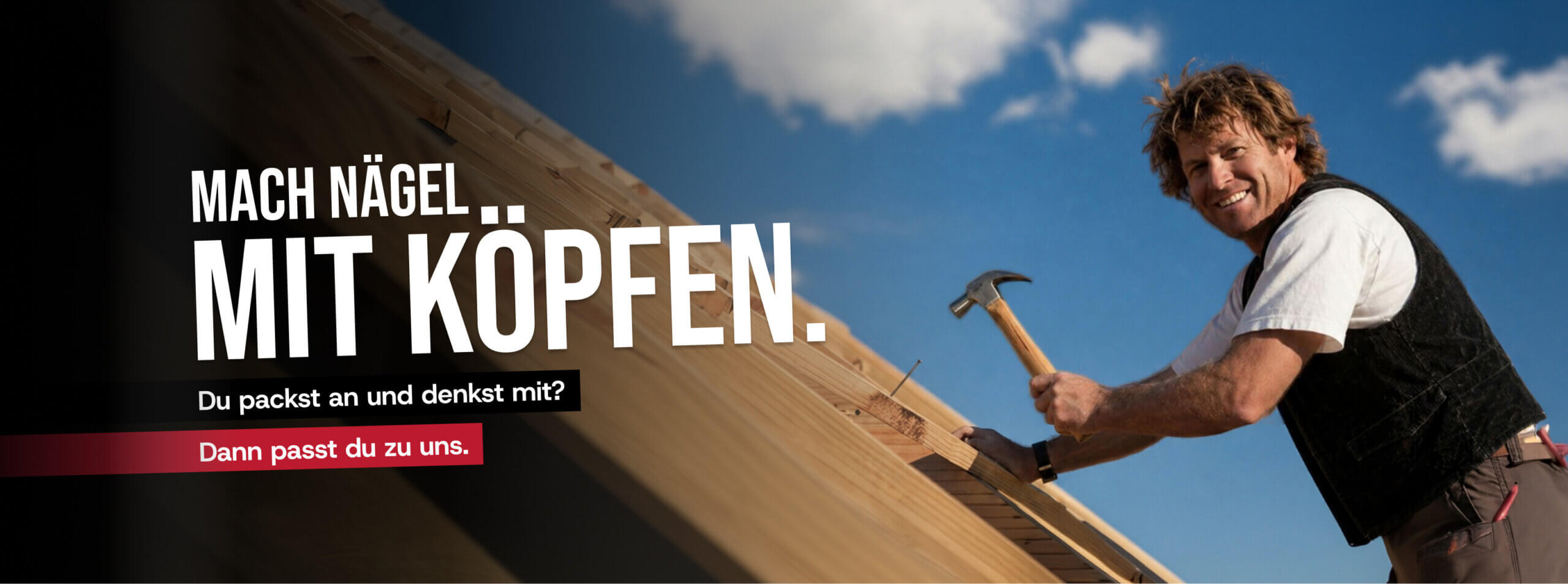 Zimmerer auf dem Dach, schlägt mit Hammer auf Holz und lächelt in die Kamera.